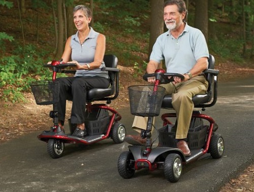 A middle-aged couple riding mobility scooters on a wooded path.