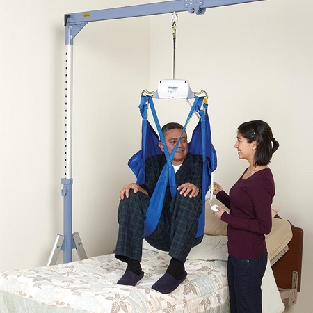 A man being lifted out of bed with a motorized patient lift. 