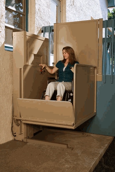 A young woman in a wheelchair lift that's mounted next to a flight of outdoor stairs.