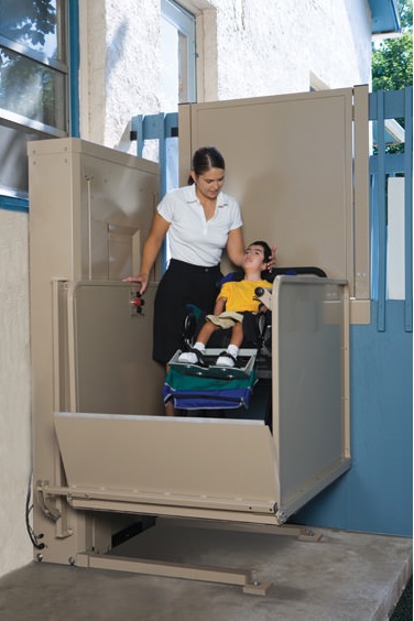 A child in a wheelchair and mother using a vertical platform lift on an outdoor porch.