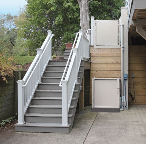 A wheelchair lift installed next to a fight of outdoor steps leading up to a raised porch.