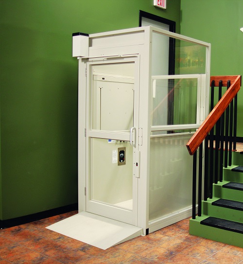 An indoor vertical platform lift next to a small flight of steps leading up to an exit door.
