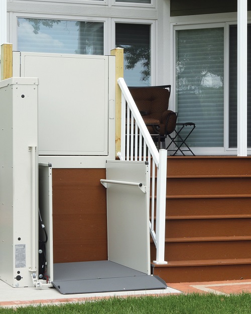 A wheelchair lift positioned next to a flight of steps leading up to a raised porch.