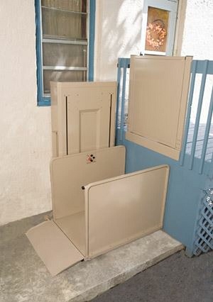 A vertical platform lift installed next to a blue staircase that accesses a back door.