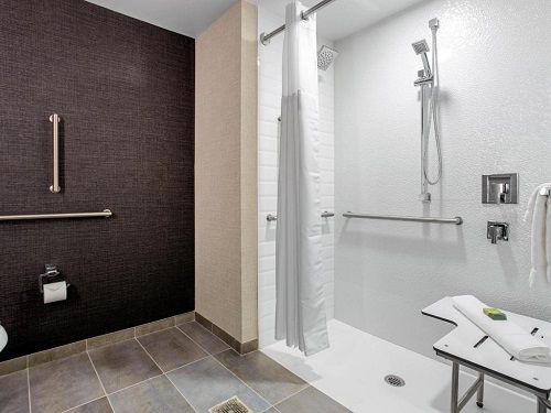 A roll-in shower with a shower rod, grab bars, and shower wand.