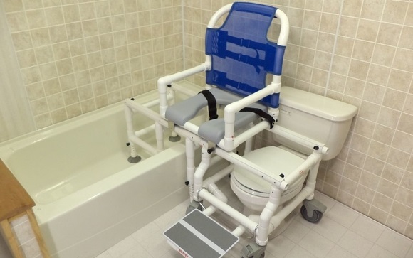A tub and toiler transfer chair in a bathroom with beige tiling.