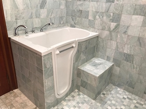 A walk-in tub with pale green marble tiling. 