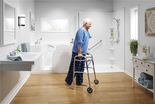 Elderly man using a walker to cross a bathroom that has a walk-in tub and roll-in shower.
