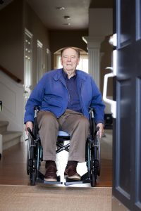 An elderly man in a wheelchair starts to exit an open house door.
