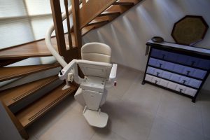 A brown staircase with a white curved stair lift in a home. 